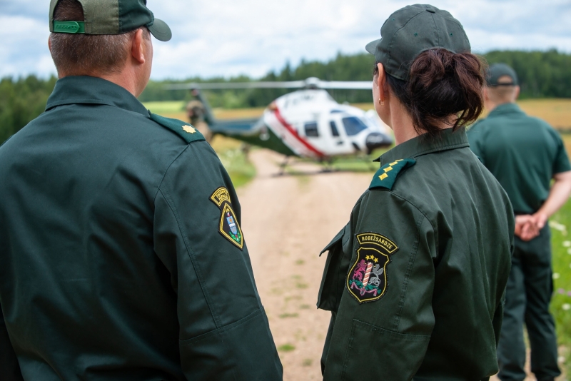 Valsts robežsardzes amatpersonas un aiz tām helikopters