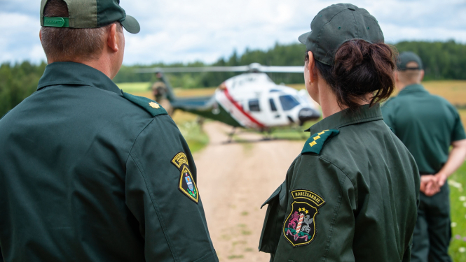 Valsts robežsardzes amatpersonas un aiz tām helikopters