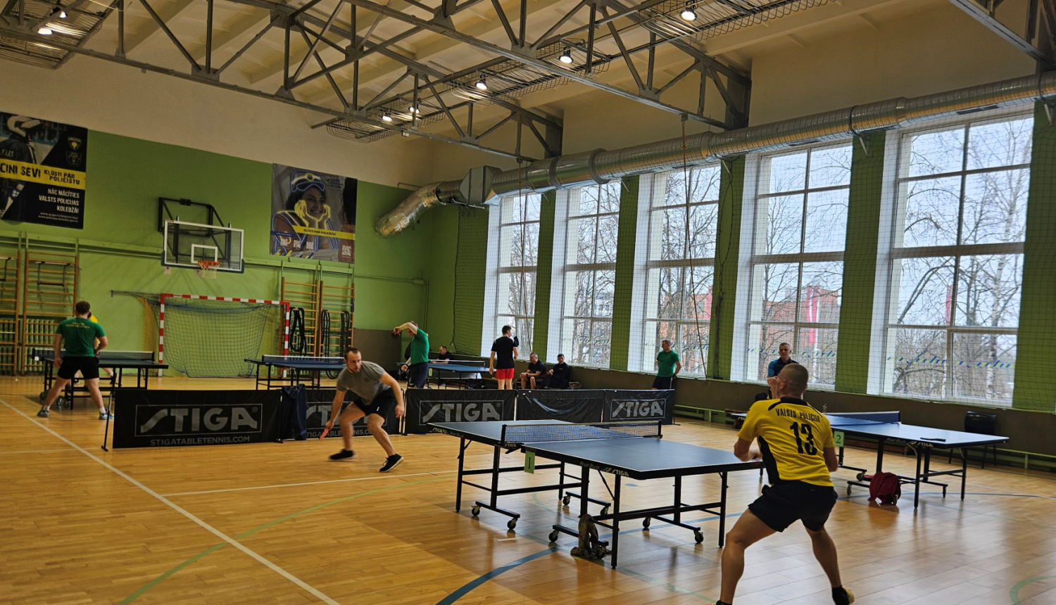 cilvēki sporta zālē spelē galda tenisu