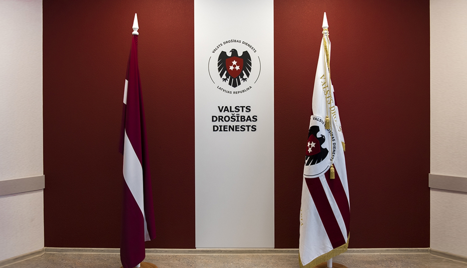 Latvijas un VDD karogi ar VDD logo fonā