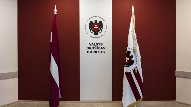 Latvijas un VDD karogi ar VDD logo fonā