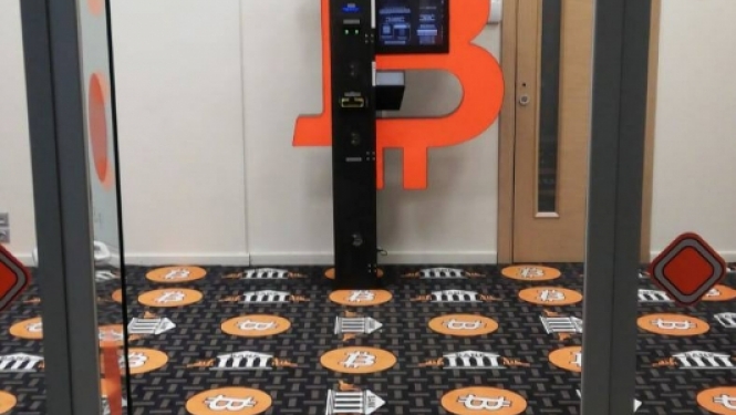 bitkoinu klubs ar lielu oranžu B burtu uz dienas un raibu paklāju uz grīdas