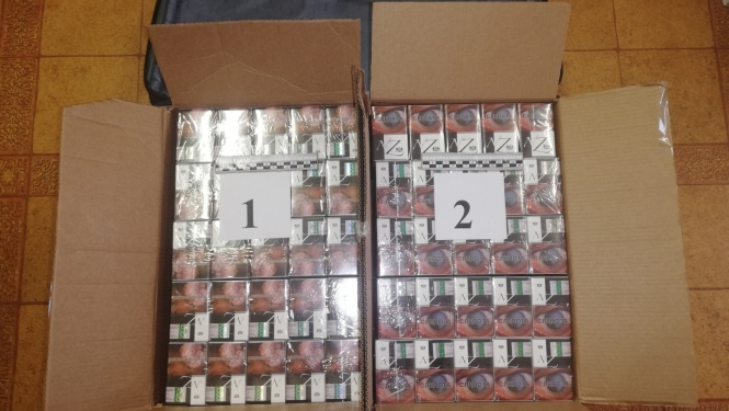 cigarešu bloki divās kartona kastēs uz galda novietoti, blakus datora soma