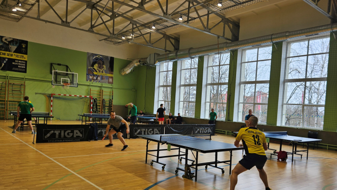 cilvēki sporta zālē spelē galda tenisu