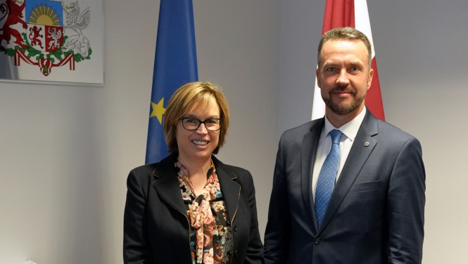 Sieviete un vīrietis priekšplānā, aiz viņiem Eiropas savienības zilais karogs un Latvijas karogs