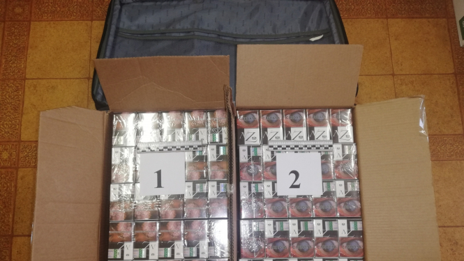 cigarešu bloki divās kartona kastēs uz galda novietoti, blakus datora soma