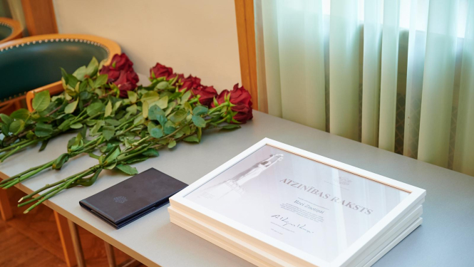 Atzinības raksti uz galda kopā ar sarakām rozēm