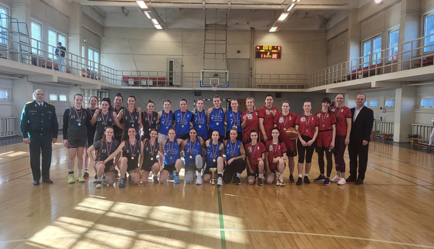 komandas stāv zālē ar medaļām