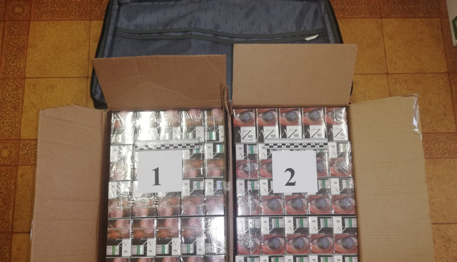 cigarešu bloki divās kartona kastēs uz galda novietoti, blakus datora soma