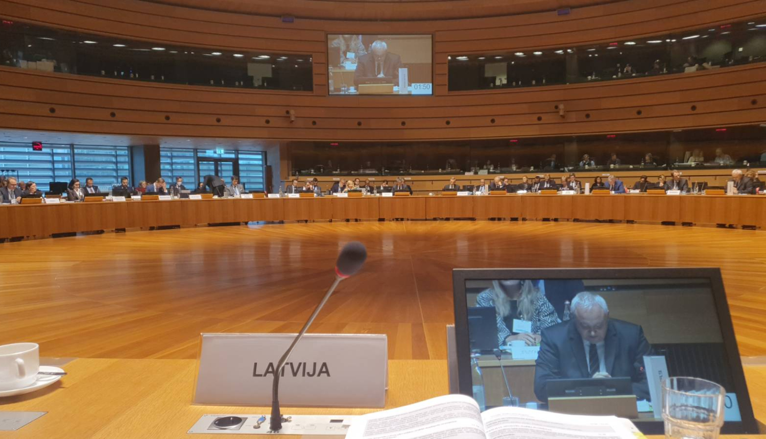 Ap apaļo galdu sēž cilvēki, priekšplānā planšetdators un mikrofons