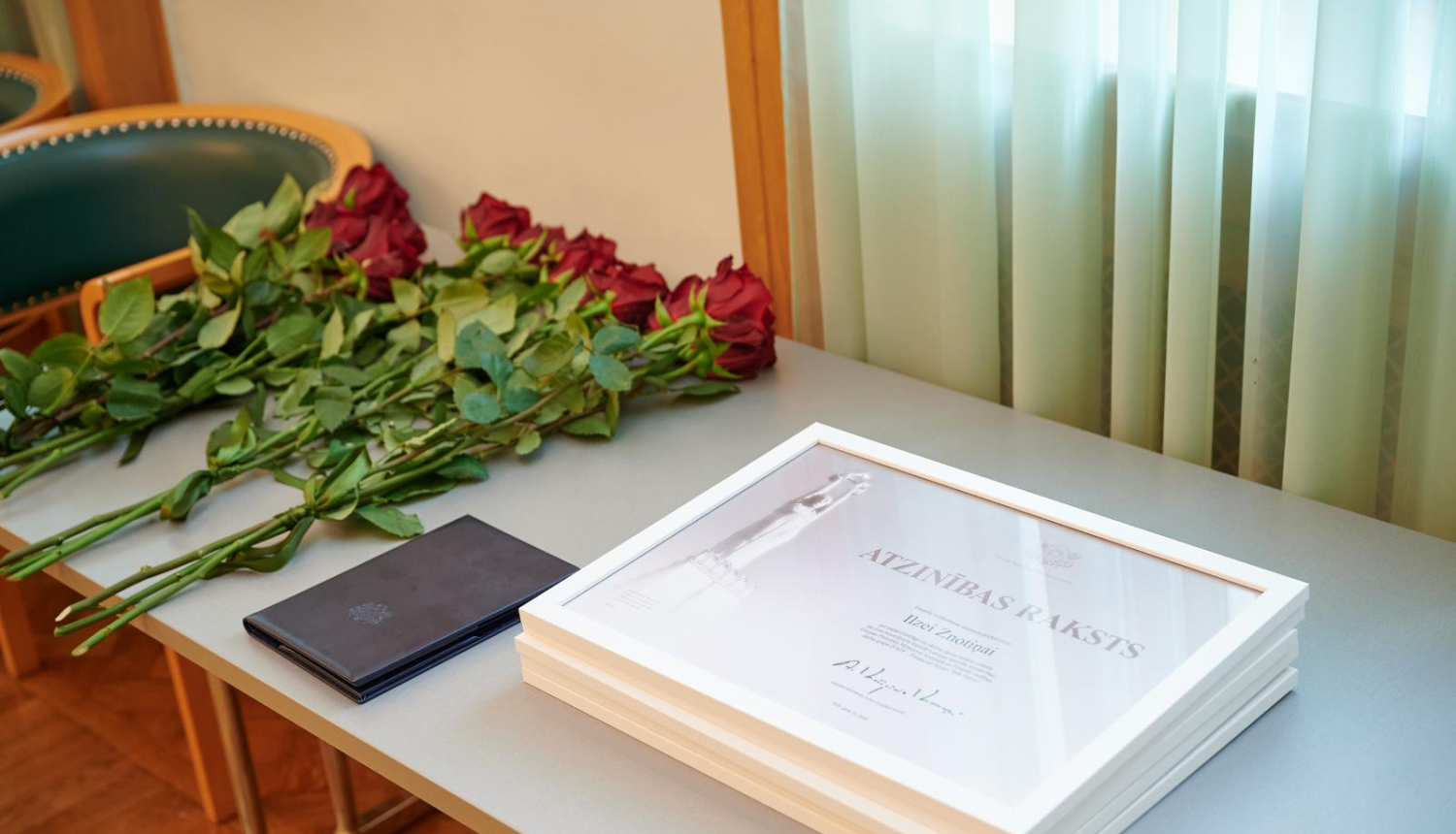 Atzinības raksti uz galda kopā ar sarakām rozēm