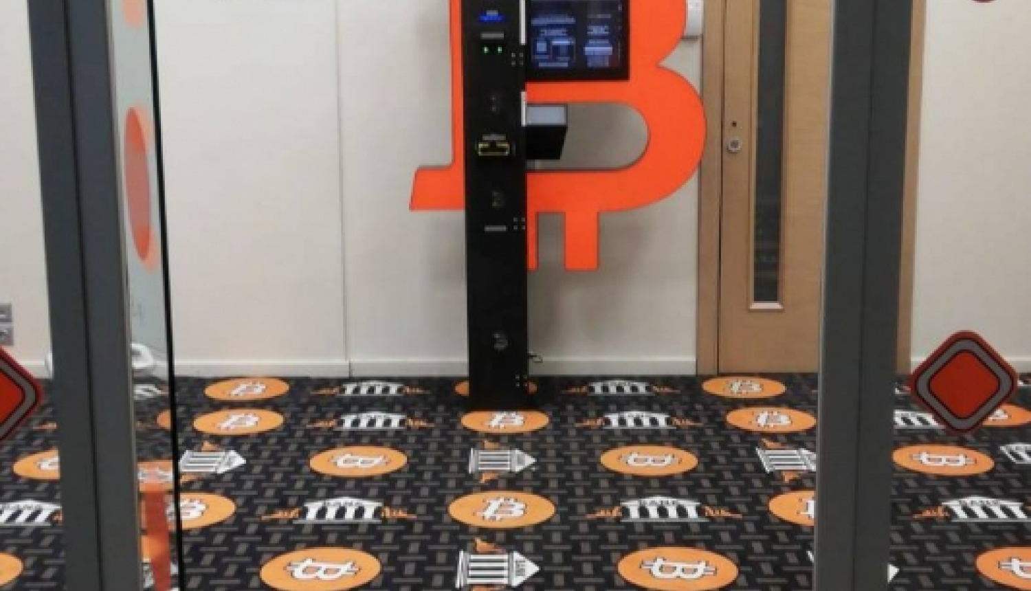 bitkoinu klubs ar lielu oranžu B burtu uz dienas un raibu paklāju uz grīdas