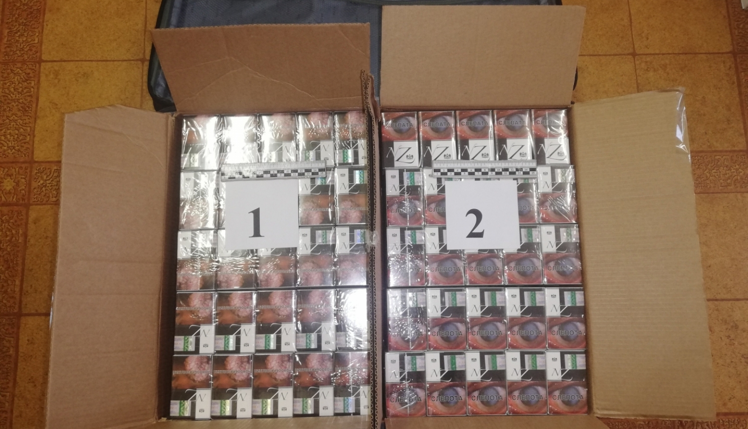 cigarešu bloki divās kartona kastēs uz galda novietoti, blakus datora soma