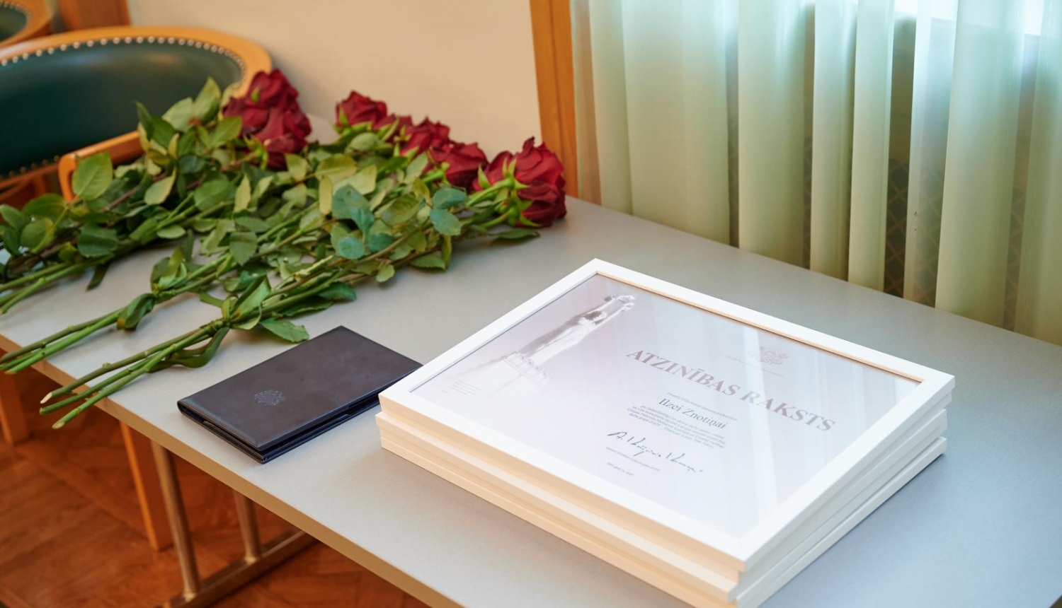 Atzinības raksti uz galda kopā ar sarakām rozēm