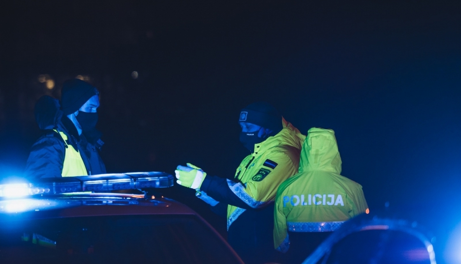 trīs policisti pie mašīnas naktī